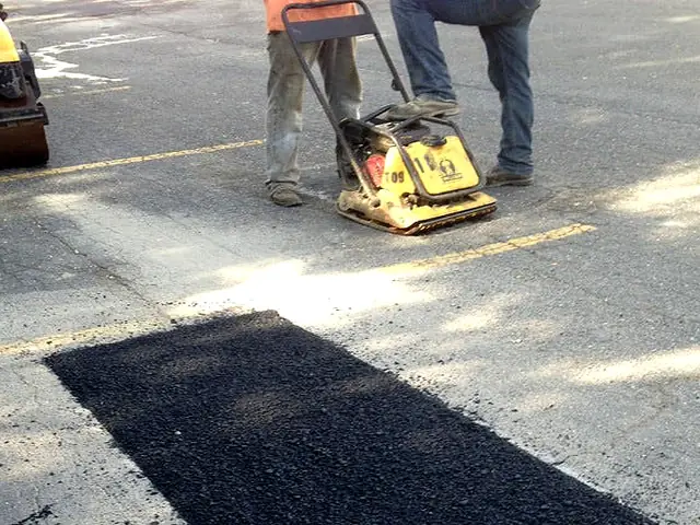A crew compacting a fresh asphalt patch on a parking lot