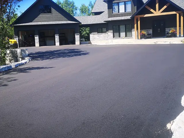 A freshly paved black asphalt driveway in front of a new home