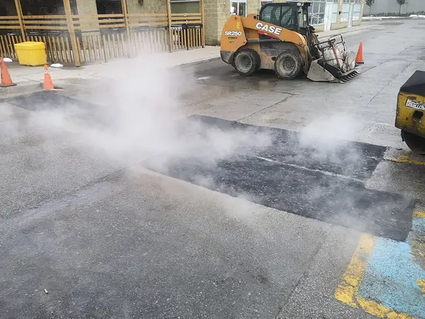 Hot asphalt being laid with steam rising on a parking lot
